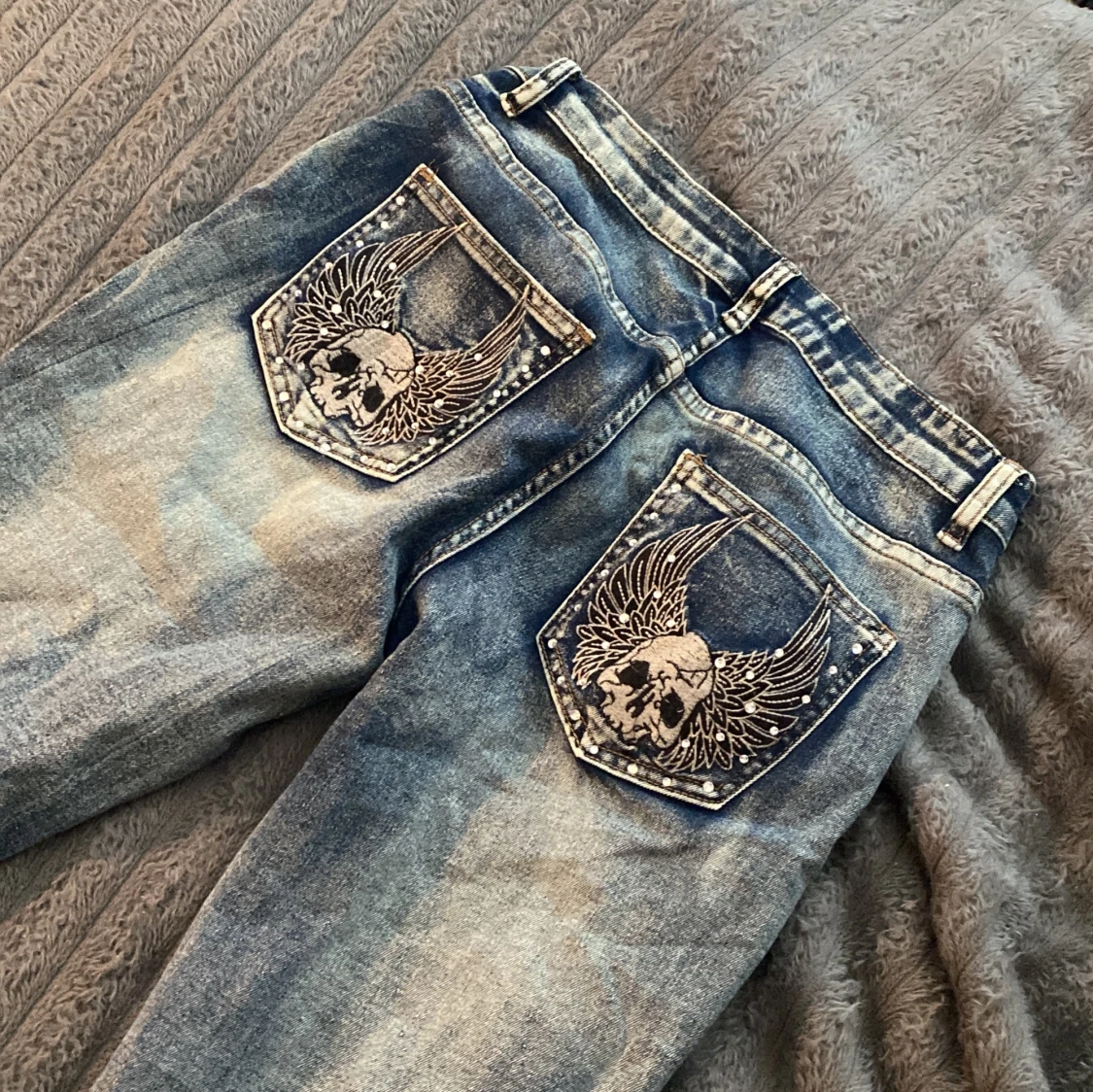 Blå jeans med dödskallebroderi på bakfickorna
