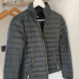 Grön dunjacka från Zara Woman - Säljer en grön dunjacka från Zara Woman med quiltad design och dragkedja framtill. Jackan har två fickor med dragkedja och en stilren, enkel look som passar till många outfits.