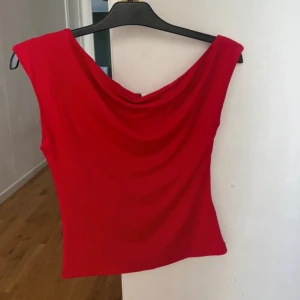 Röd oneshoulder topp - Säljer en snygg röd oneshoulder topp med draperad halsringning. Perfekt för dig som vill sticka ut med en färgstark och trendig look. Tunn och mjuk kvalitet som sitter skönt på kroppen. Nysick 