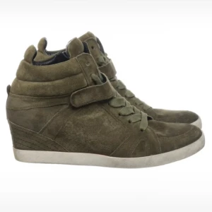 Olivgröna sneakers med kilklack - Säljer ett par olivgröna sneakers med kilklack och snörning. Skorna har en bred kardborre över vristen och är gjorda i mocka. Snygg och sportig look med vit sula och rund tå. Det är i väldigt bra skick då det knappt är andvända öppen för affär vid snabbt köp 💕