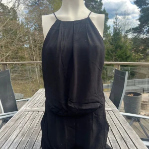 Svart klänning med spetsrygg från Samsøe Samsøe - Säljer en svart jumpsuit från Samsøe Samsøe! Den har tunna axelband och en enkel rak halsringning. Baksidan är superfin med en spetsdetalj som ger en snygg öppen rygg. Och den har fickor på sidorna vilket är så praktiskt!