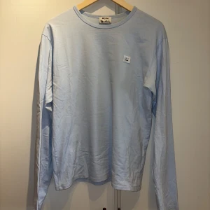 Ljusblå långärmad t-shirt från Acne - Svinsnygg långärmad t-shirt från Acne i stl. S. Något oversized. Köpt på NK 2017, använd några gånger men har sen bara legat i garderoben. Ärmarna är bredare och längre jämfört med vanliga långärmade t-shirts och den var väldigt eftertraktad säsongen den släpptes. Broderad square face-logga på bröstet.