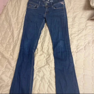 Blå Replay jeans med bootcut - Säljer ett par klassiska blå jeans från Replay med bootcut passform. Jeansen har fem fickor, snygga kontrastsömmar och en liten röd Replay-logga på bakfickan. Perfekta till vardags och lätta att matcha med olika stilar.