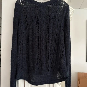 Marinblå  stickad tröja  - Säljer en marinblå stickad tröja i storlek L. Tröjan har ett genombrutet mönster framtill och långa ärmar. Perfekt att styla med jeans eller kjol för en snygg look.