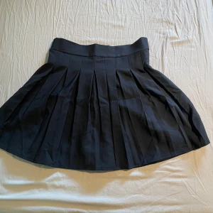 Svart plisserad kjol från Qesto - Säljer en svart plisserad kjol från Qesto i storlek M. Kjolen har bred linning och klassiska veck som ger en snygg och tidlös look. Perfekt att styla med en enkel topp eller hoodie.