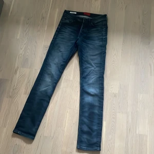 Mörkblå slim jeans från Jack & Jones - Snygga mörkblå slim fit jeans från  Jack & Jones med  diskreta slitningar framtill. Jeansen har normal midja och raka ben, perfekta till vardags. Märke syns på insidan av linningen.