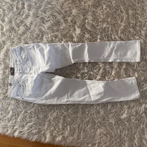 Vita jeansbyxor från Morris - Säljer ett par fräscha vita jeansbyxor från Morris. Klassisk femficksmodell med raka ben och normal passform. Byxorna har silverfärgade nitar och detaljer samt bälteshällor i midjan. Perfekta för en stilren look.