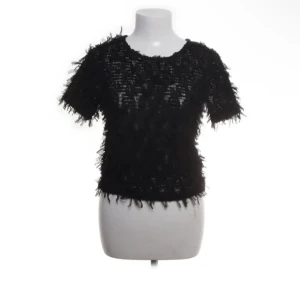 Svart topp med fransdetaljer från Zara - Säljer en svart topp från Zara med korta ärmar och unika fransdetaljer över hela tyget. Toppen har en rund halsringning och är tillverkad i ett genombrutet material som ger en cool och trendig look.