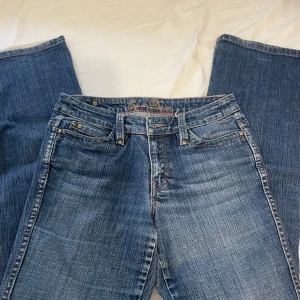 Blå jeansbyxor från Esprit med broderade bakfickor - Säljer ett par klassiska blå jeansbyxor från Esprit med snygga broderade detaljer på bakfickorna och guldiga knappar. Byxorna har regular passform och fem fickor. Perfekta till vardags för en avslappnad stil.