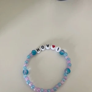 Färgglatt pärlarmband med text - Sött armband med pärlor i blått, rosa och vitt. Armbandet har bokstavspärlor som bildar texten 'HOV❤️1' med ett rött hjärta. Perfekt accessoar för att ge en personlig touch till din stil. Hov1 inspirerat ❤️