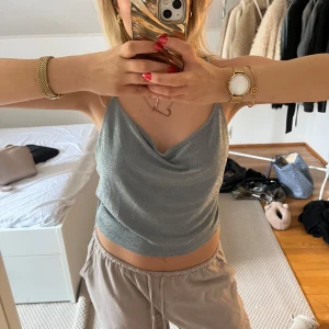 Glittrig silver topp med öppen rygg - Säljer en glittrig silvergrå topp med draperad urringning och tunna axelband som korsas och knyts i ryggen. Toppen har en öppen rygg och är i utmärkt skick.