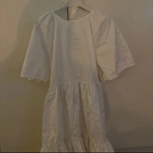 Vit klänning med volang från Glamorous - Säljer en vit klänning från Glamorous med volang nertill och knytband i ryggen. Klänningen har korta, vida ärmar och en luftig passform. Perfekt för varma dagar eller speciella tillfällen.