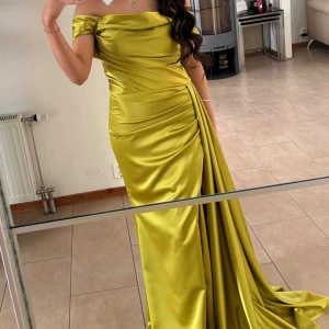 Limegrön långklänning i satin - Säljer en elegant limegrön långklänning i glansigt satinmaterial. Klänningen har offshoulder-modell, draperade detaljer och en lång släp. Perfekt för bal eller festliga tillfällen.