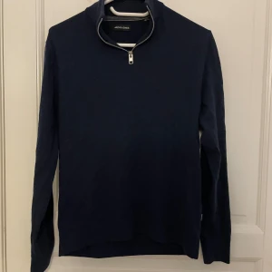 Mörkblå tröja med dragkedja från Jack & Jones - Säljer en stilren mörkblå långärmad tröja från Jack & Jones med halv dragkedja vid halsen. Perfekt för lager-på-lager och enkel att matcha med olika outfits. Storlek XS