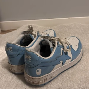 BAPE STA sneakers i blå o Vit - Säljer ett par BAPE STA sneakers i blått och vitt med klassisk stjärndesign på sidan. Skorna har snörning, rund tå och platt sula. Ovandelen är i blank syntet med vita detaljer och BAPE-logga på hälen och tungan. Är få gånger använd så är i helt ny skick dessutom nypris på ca 2800kr är storlek 43.