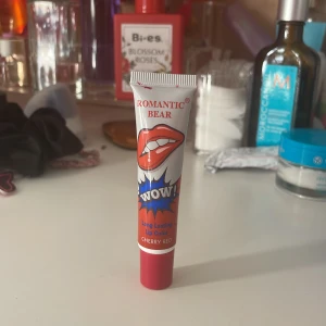 Romantic Bear WOW! Long Lasting Lip Color Cherry Red - Romantic Bear WOW! Long Lasting Lip Color i färgen Cherry Red. Tuben har ett färgstarkt rött och vitt tryck med läppmotiv. Produkten är en flytande läppfärg som ger intensiv röd nyans och långvarigt resultat.