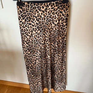 Ny Leopardmönstrad långkjol från Vila - Säljer en snygg långkjol från Vila med leopardmönster. Kjolen har en rak passform och resår i midjan för extra komfort. Perfekt för dig som vill sticka ut med ett djurmönstrat plagg. •Material: 100% polyester. Mycket lätt och snygg. •Tyg: satin. •Storlek: 34. •Köpte för 429 kr. •Djurfritt och rökfritt hem.