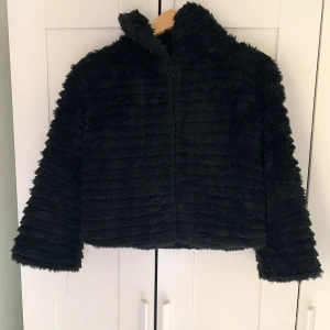 Svart Croppad jacka i fuskpäls  - Svart croppad jacka i fuskpäls Storlek M men passar som S. Den har två gömda krokar längst fram så att det går att stänga jackan. 