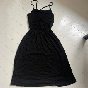 Svart sommarklänning med smala axelband - En enkel svart klänning med smala axelband korsade i ryggen och resår i midjan. Klänningen är ärmlös och har en luftig passform, perfekt för varma dagar. Kan användas till stranden eller som en vanlig vardagsklänning. Längden är mellan knä och vad. Knappt använd. Skriv för fler bilder💞 