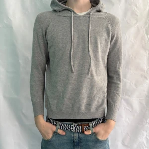 Grå merinoull hoodie - Säljer en stilren grå merinoull hoodie med dragsko i huvan. Tröjan har lång ärm och är tillverkad i ett mjukt material som passar perfekt för kyligare dagar. Enkel och tidlös design som funkar till det mesta.