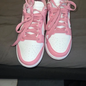 Nike Dunk Low rosa och vita sneakers - Säljer ett par Nike dunk. Jag har använt dem 1 gång och kunde inte lämna tillbaka dem. De är från zalando. Har kvar originalförpackningen. Stl 38. Perfekta för dig som vill sticka ut med en snygg och trendig look.