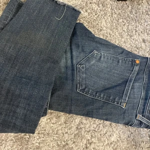 Mörkblå super skinny jeans från H&M - Säljer ett par mörkblå super skinny jeans från H&M med låg midja. Jeansen har klassisk femficksdesign, dragkedja och knapp framtill samt råa benslut. Perfekta för dig som gillar en tight passform.