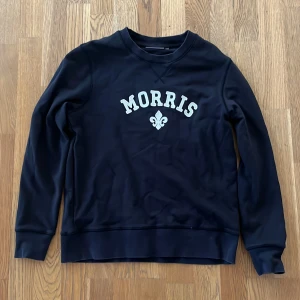 Mörkblå sweatshirt från Morris - Snygg mörkblå sweatshirt från Morris med vit text och logga framtill. Tröjan har rund halsringning och långa ärmar, perfekt för en avslappnad stil. Klassisk och enkel design som passar till mycket.
