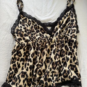 Leopardmönstrad linne med spetsdetaljer - Säljer ett leopardmönstrat linne med svarta spetsdetaljer längs kanterna och v-ringning. Linnet har smala axelband och är perfekt för dig som vill sticka ut lite extra.