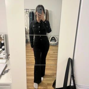 Svart jeansoverall/jumpsuit - Säljer en svart jeansoverall/jumpsuit med klassisk krage och silverfärgade knappar framtill. Jackan har två bröstfickor med lock och knappar samt långa ärmar. Supersnygg till både vardag och fest. Köpt från en tjej på Plick men tyvärr var detta inget för mig. 