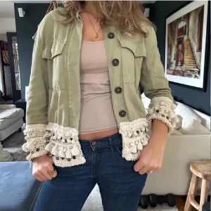 Grön jacka med fransar från Zara! - (Priset går att diskutera) Snygg ljusgrön jacka med stora virkade detaljer och tofsar längs ärmslut och nederkant. Jackan har stora knappar framtill och två bröstfickor. Mycket trendig just nu. Storlek XS men passar många olika beroende på hur man vill att den ska sitta!!
