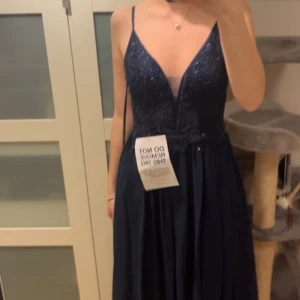 Marinblå festklänning/balklänning med glitter från Mascara London - Jag säljer min marinblå balklänning från Mascara London med glittrig överdel och djup v-ringning. Klänningen har smala axelband och ett elegant fall i kjolen. Den har inte används och har fortfarande prislappen kvar, nypris egentligen 2100kr, men nu nedsatt till 1900kr. Köpte den på Zalando men Mascara är märket☺️Den är perfekt för bal, men funkar också till andra festliga tillfällen. Det är bara att höra av sig för mer bilder eller om du har prisförslag eller frågor! 