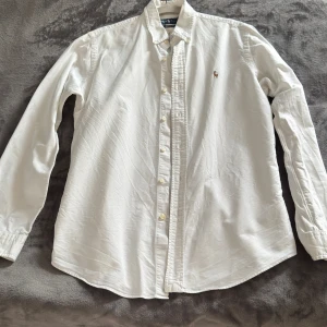 Vit skjorta från Ralph Lauren - Fin vit skjorta från Ralph Lauren med brun logga på bröstet. Enkel vilket gör det perfekt för alla tillfällen.