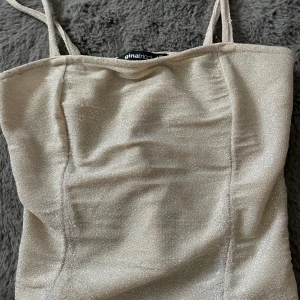 Glittrig beige linnetopp från Gina Tricot - Säljer en glittrig beige linnetopp från Gina Tricot med smala axelband. Toppen har en figurnära passform och skimrande material som ger en snygg look.