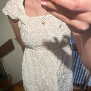 Vit klänning med broderade volangärmar - Säljer en söt vit klänning med broderade detaljer och volang vid axlarna. Klänningen har en feminin passform och är ärmlös med spetsinslag. Perfekt för skolavslutningen, midsommar eller student!