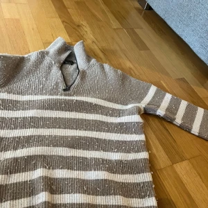 Beige och vit randig stickad tröja från Massimo Dutti - Säljer en stickad tröja från Massimo Dutti i beige och vitt med breda ränder. Tröjan har halv dragkedja vid halsen och ribbade muddar. Perfekt för kyliga dagar och har en klassisk look.