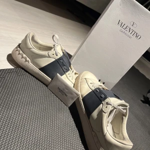 Valentino Garavani sneakers  - Snygga sneakers från Valentino Garavani i vitt med bred svart panel över sidan. Skorna har rund tå, platt sula och klassisk snörning. Perfekta för dig som gillar stilrena och exklusiva sneakers med en modern touch. Kan inte lova att dom är äkta men han jag köpte dom av sa att dom var det!