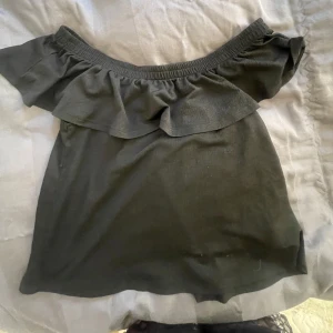 Svart offshoulder topp med volang - Snygg svart offshoulder topp med bred volang runt axlarna. Perfekt för en trendig och stilren look. Toppens material känns mjukt och följsamt mot huden. Passar mig som brukar ha S 