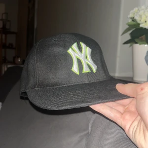 Svart New Era Yankees keps - Säljer en svart New Era 59FIFTY keps med New York Yankees-logga i vitt och limegrönt framtill. MLB-logga baktill. Klassisk rak skärm och broderade detaljer. Perfekt för dig som gillar sportig stil.