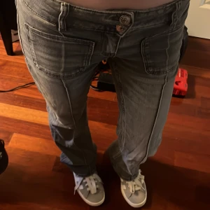 Grå jeansbyxor med raka ben - Säljer ett par grå jeansbyxor med bootcut och stora framfickor. Byxorna har låg midja och klassisk femficksdesign med dubbla knappar framtill. Perfekta för en avslappnad och trendig look.