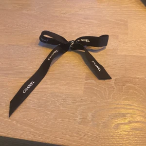 Svart rosett från Chanel - Säljer en svart dyrbar rosett från Chanel med vit logotyptext längs hela bandet. perfekt för att ge en exklusiv touch till din outfit.    Ordinarie pris: 37 049 kr och är jätte fin i håret!!!😊☺️