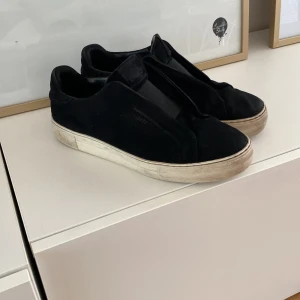Axel Arigato - Svarta sneakers från Axel Arigato i mocka med bred resår över vristen och vit platt sula. Snygg minimalistisk design utan snörning, perfekt för en stilren look.