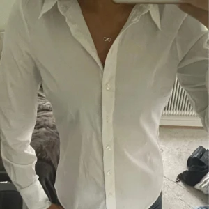 Vit skjorta från H&M - Klassisk vit skjorta från H&M i bomull. Skjortan har lång ärm, krage och knäppning framtill. Perfekt till jeans eller kostymbyxor för en clean och stilren look. Har använt den en gång till en skolgrej och köpte den för 400kr🩷🩷
