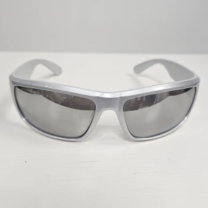 Silvriga sportiga solglasögon - Coola solglasögon med silvrigt båge och spegelblanka linser. Modellen har en sportig, svepande form som täcker bra runt ögonen. Perfekta för dig som gillar en futuristisk look och vill sticka ut.