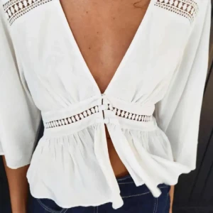 Vit blus Zara - Säljer en vit blus med djup v-ringning i ryggen och fina spetsdetaljer vid axlar och midja. Blusen har trekvartsärm och knytning i midjan för en snygg passform. Perfekt till jeans eller kjol!