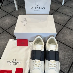 Valentino Garavani sneakers - Säljer ett par vita Valentino Garavani sneakers med bred mörkblå över mitten. Skorna är perfekta nu inför sommaren. Allt på bilderna ingår!