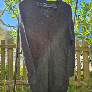 Svart stickad v-ringad lång tröja/klänning - En svart stickad tröja/klänning med v-ringning och långa ärmar. Perfekt för lager-på-lager och enkel att matcha med olika outfits. Klassisk och stilren design.