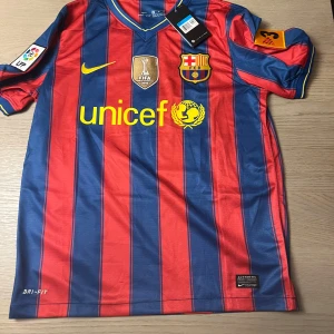 FC Barcelona Messi 10 hemmatröja - Klassisk FC Barcelona hemmatröja med Messi 10-tryck på ryggen. Röd och blå med gula detaljer, klubbmärke och Nike-logga på bröstet. DRI-FIT-material för bra komfort. UNICEF-logga på framsidan och La Liga-märke på ärmen.