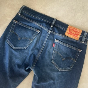 Vintage Levis 511  - Säljer ett par klassiska Levis 511 jeans i mörkblå denim. Byxorna har fem fickor, orange sömmar och Levis ikoniska läderpatch bak i midjan. Modellen är straight med normal passform och medelblå tvätt.