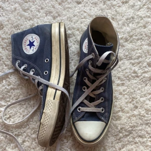 Blå Converse Chuck Taylor All Star high-tops - Klassiska blå Converse Chuck Taylor All Star high-tops med vit tå och sula. Skorna har snörning och den ikoniska loggan på sidan. Perfekta för en avslappnad och cool stil.