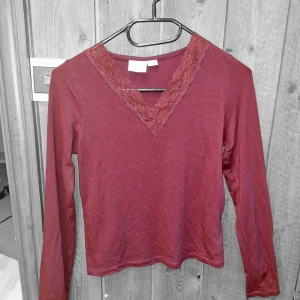Vinröd långärmad topp med spetsdetalj - Vinröd långärmad topp med v-ringning och spetsdetalj längs halsringningen. Tunn och mjuk, perfekt för lager-på-lager eller som den är. Snygg och enkel att matcha till olika outfits. En enkel tröja att ha till sommaren🌼